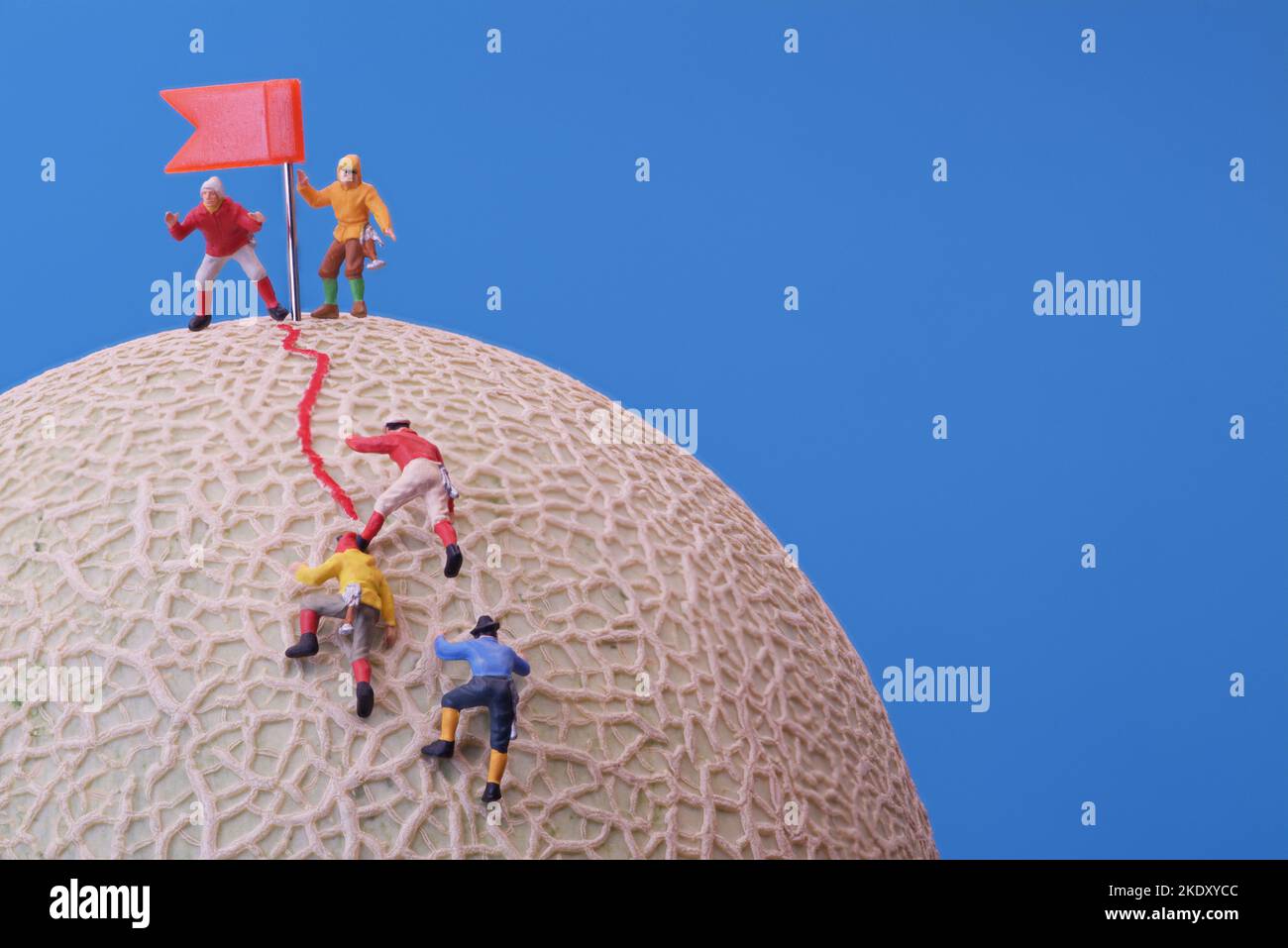 Juguetes en miniatura - Un grupo de escaladores de montaña que llegan a la cima. La fruta del melón de la roca como la base. Foto de stock