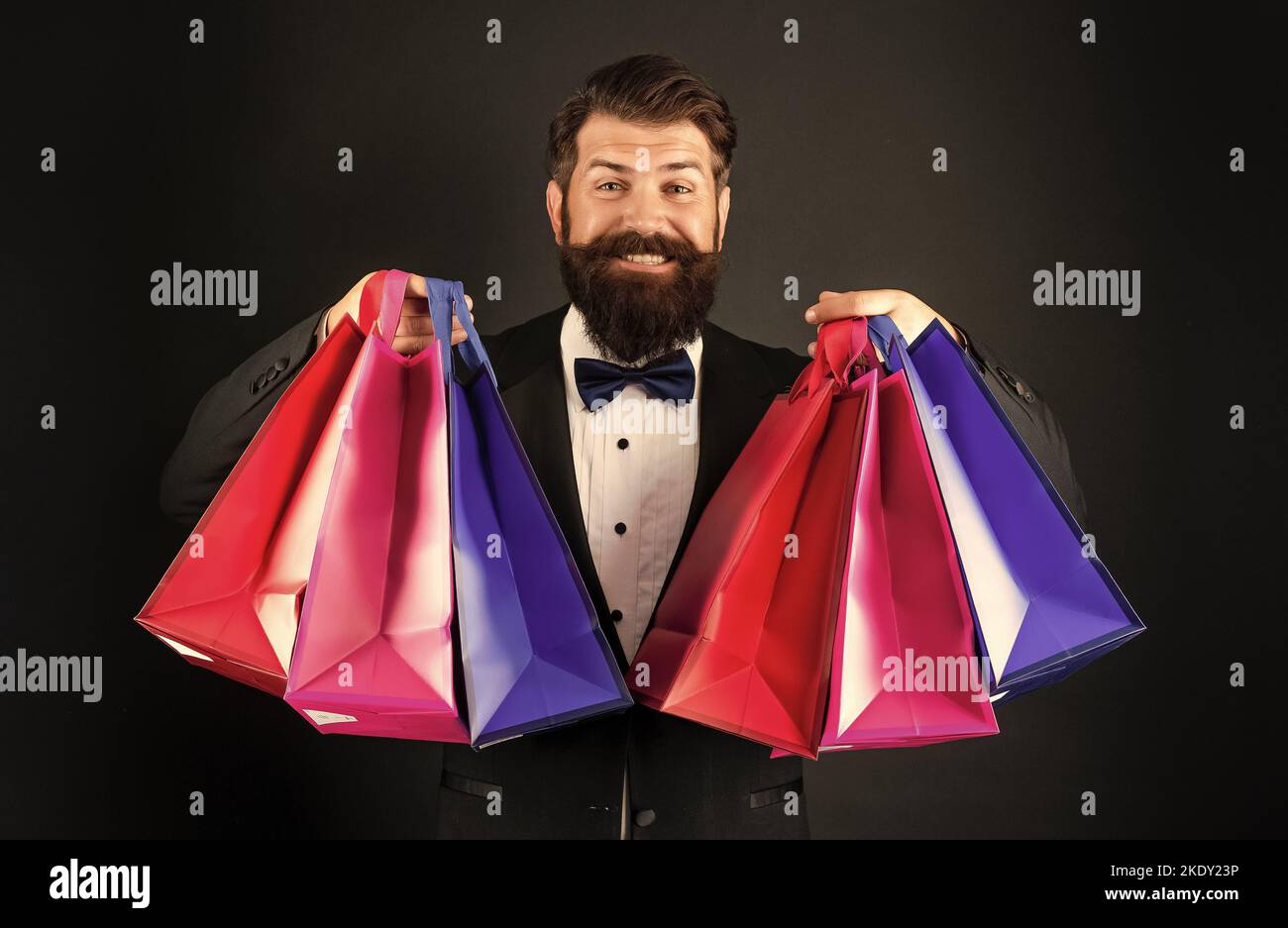 hombre feliz en el lazo de esmoquin corbata ropa de formalwear sobre fondo  negro que sostiene la compra bolsos de compras Fotografía de stock - Alamy