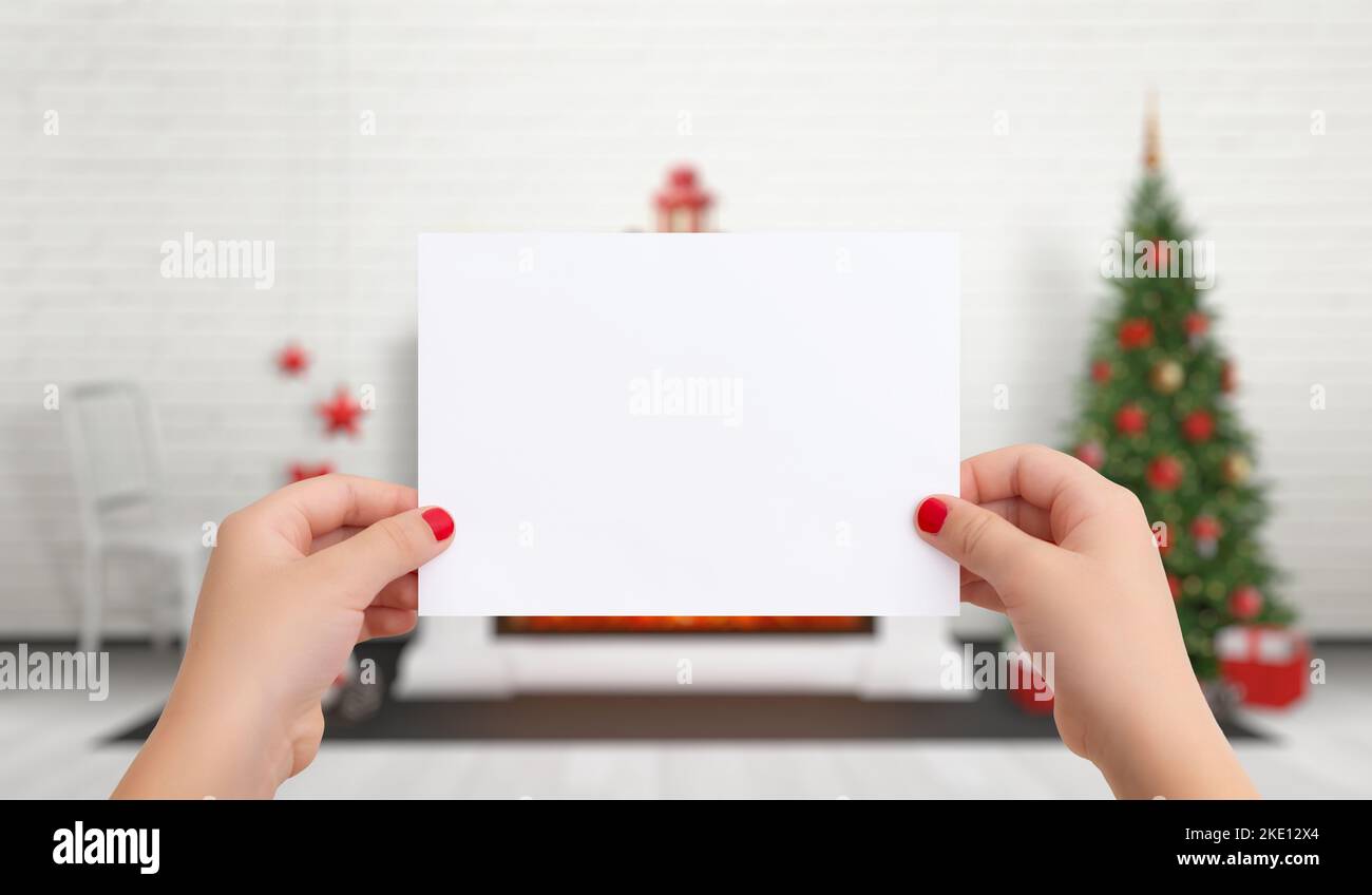 Papel en blanco para Navidad Año Nuevo tarjeta de felicitación en manos femeninas. En el fondo hay un árbol de Navidad con decoraciones Foto de stock