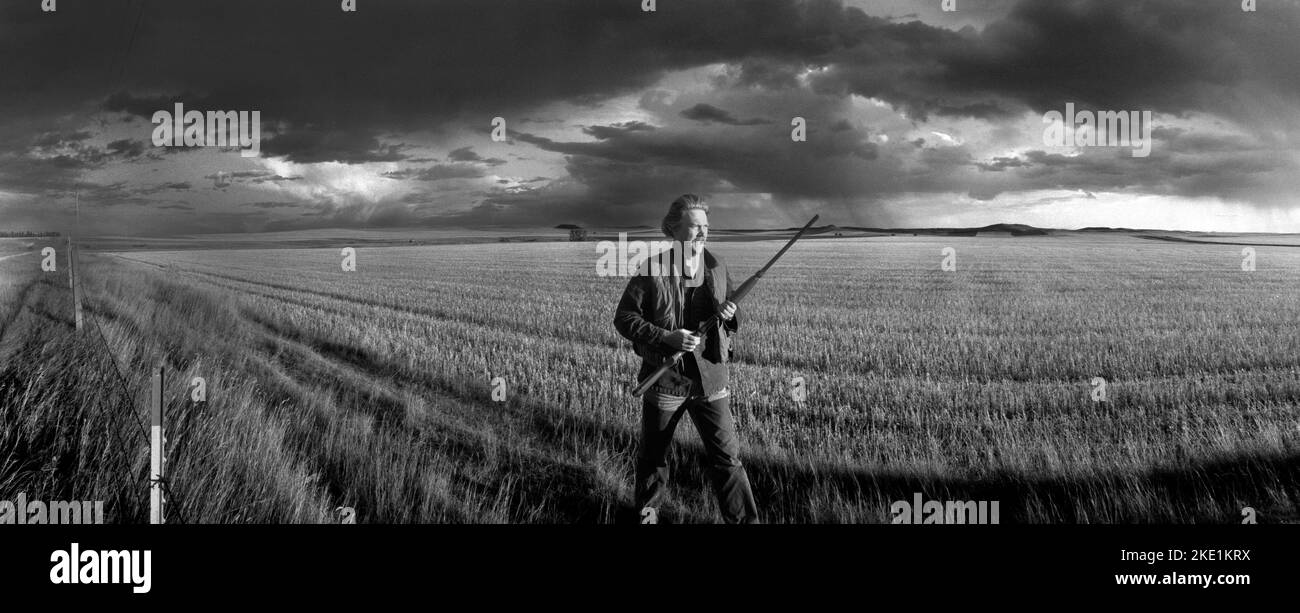 Paisaje con un cazador de tierras altas que lleva una escopeta mientras caza aves en el condado rural de Stark, Dakota del Norte en un día tormentoso y ventoso. Foto de stock