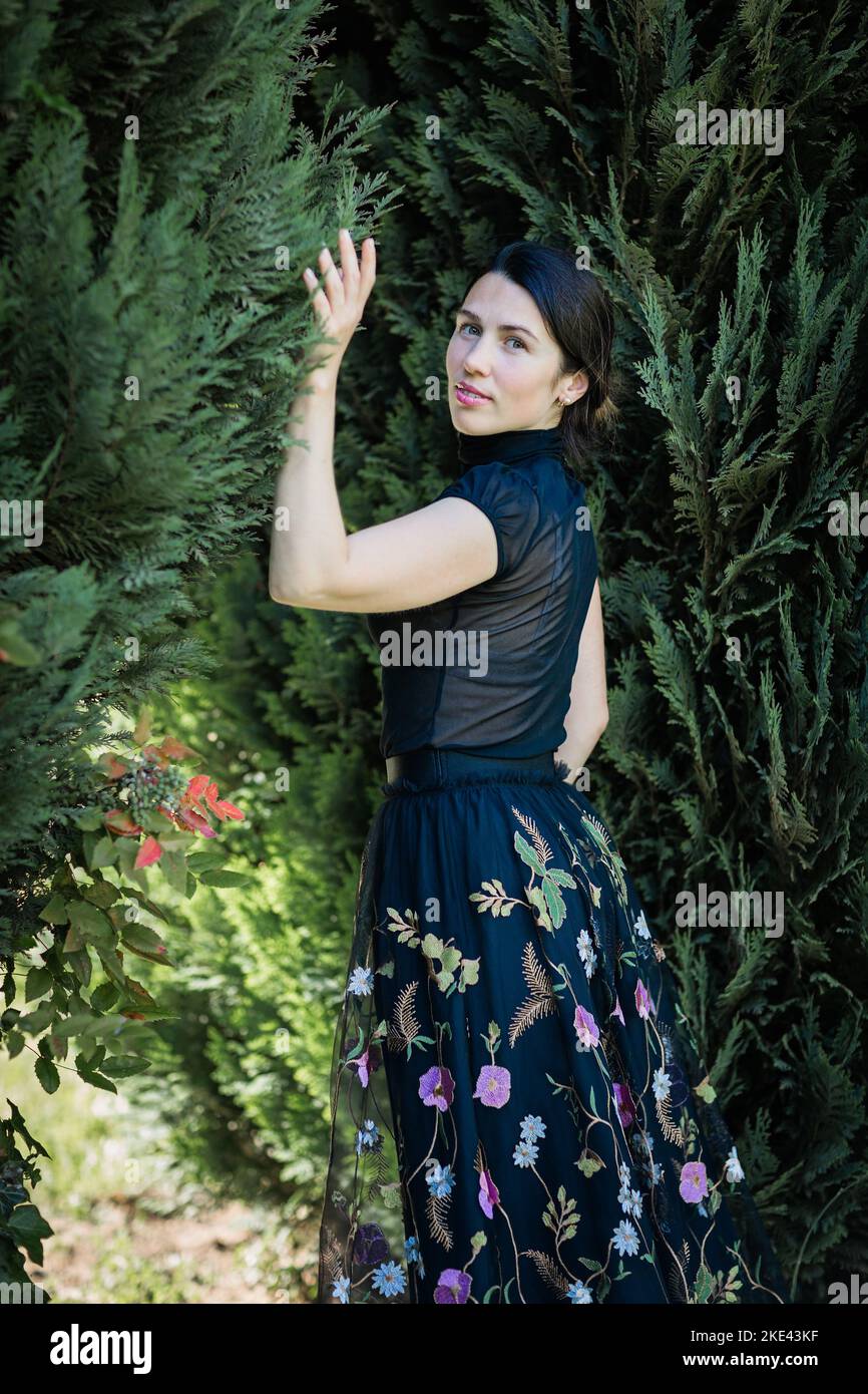 Una mujer joven con ropa negra está de pie cerca de un arbusto Foto de stock