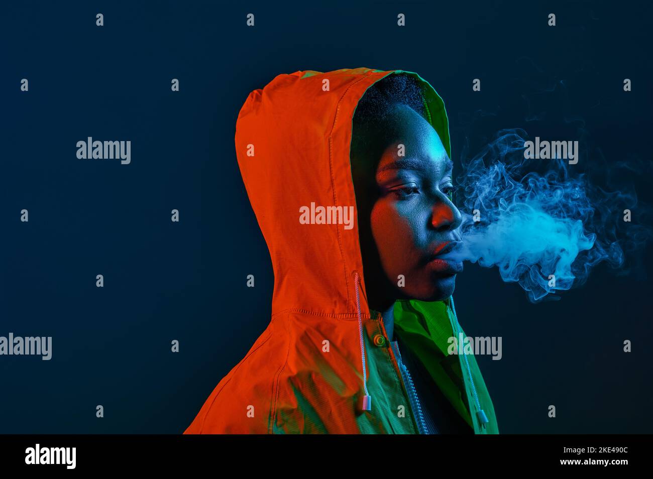 Hipster mujer en impermeable soplando humo de la boca Foto de stock