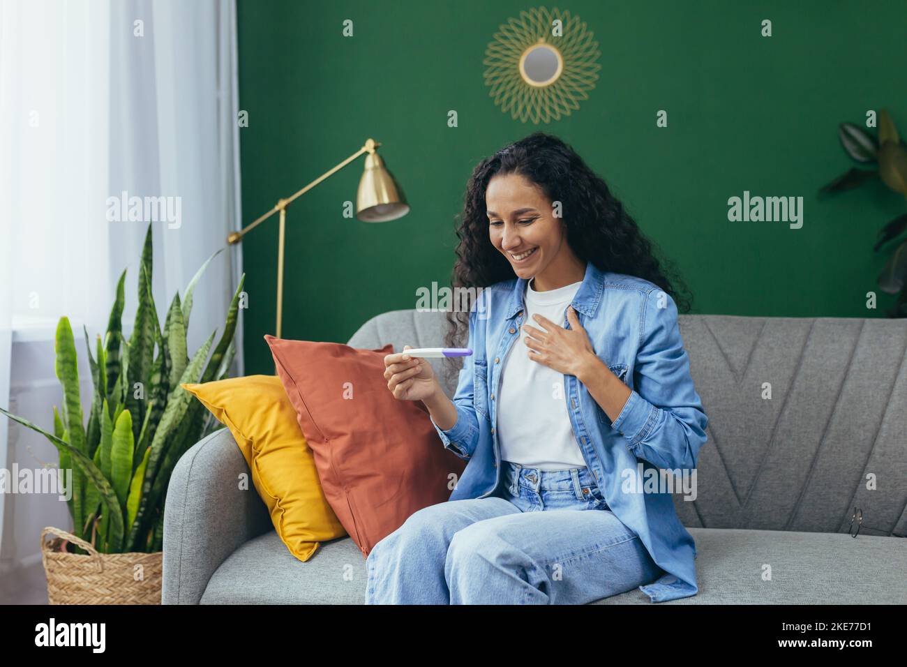 Mujer feliz sola en casa Feliz con el resultado de la prueba de embarazo, mujer hispana sola en casa sentada en un sofá en la sala de estar. Foto de stock