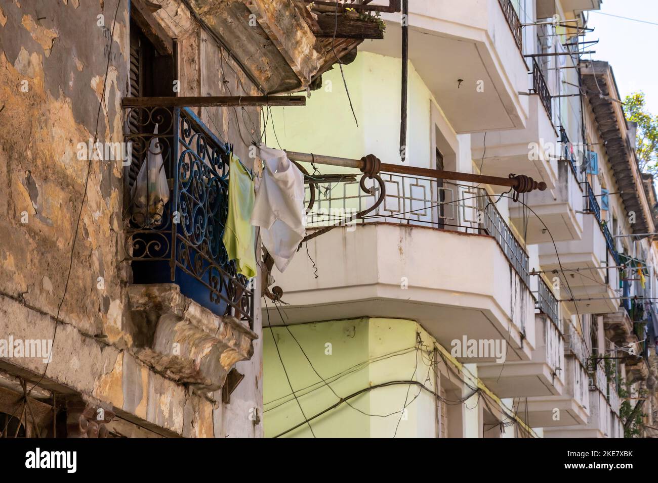 Un antiguo balcón en un edificio ruinoso, desgastado y deteriorado que contrasta con un edificio de apartamentos normal en el fondo Foto de stock