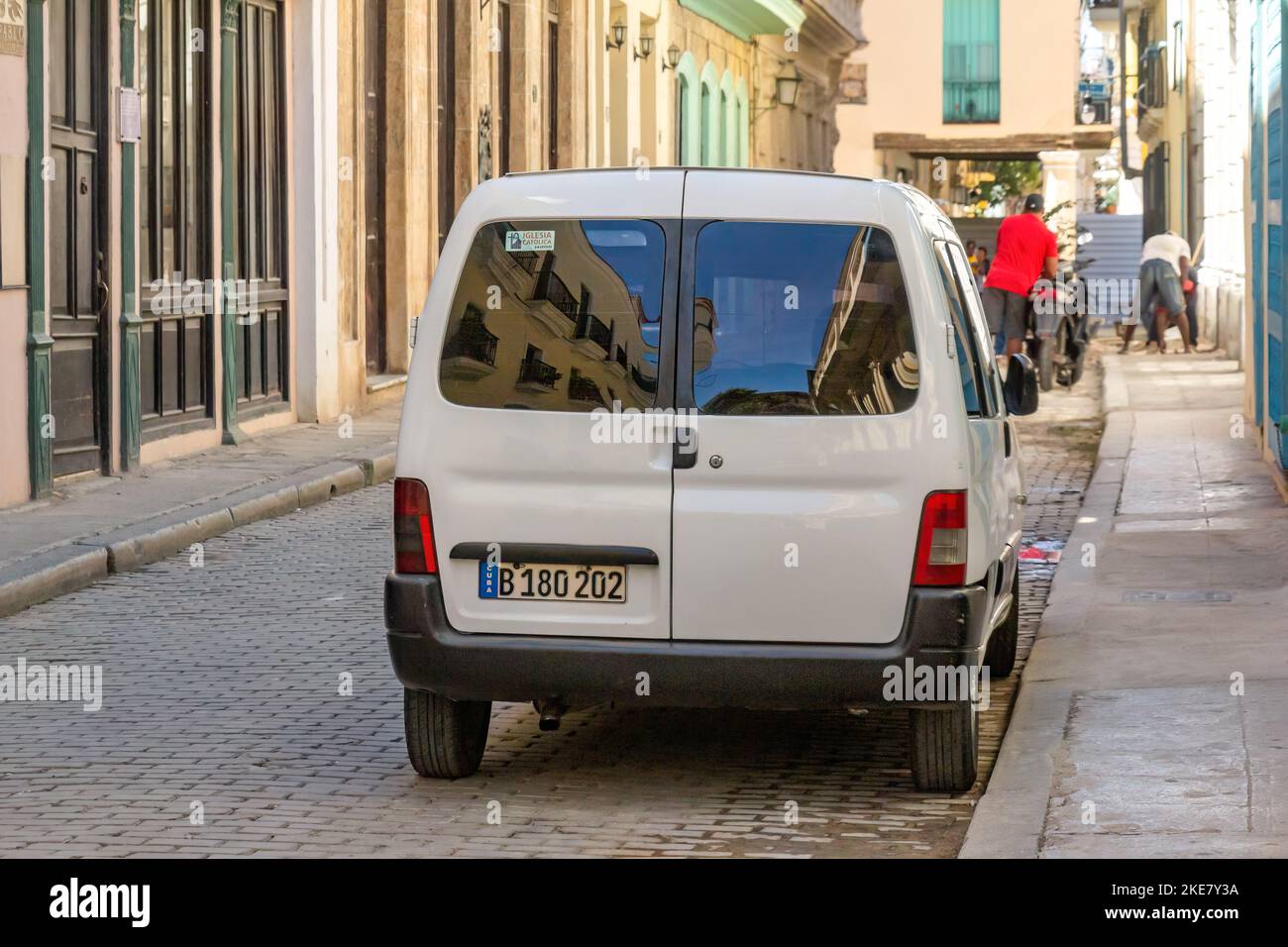 Una moderna furgoneta está aparcada en una calle adoquinada de La Habana Vieja. En el fondo, un hombre trabaja en una sección rota de la acera Foto de stock