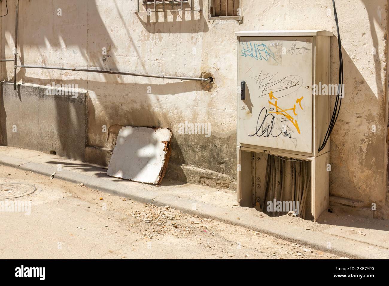 Caja de control eléctrico con graffiti en una calle sucia y pared lateral del edificio. Foto de stock