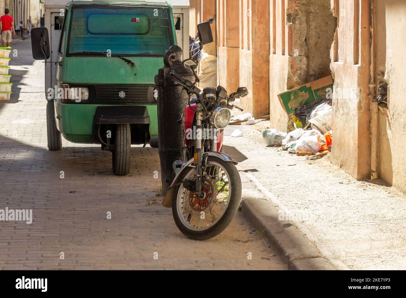 Una motocicleta y otro vehículo pequeño están estacionados en La Habana Vieja. Hay un montón de basura en la acera y entre los edificios. Foto de stock
