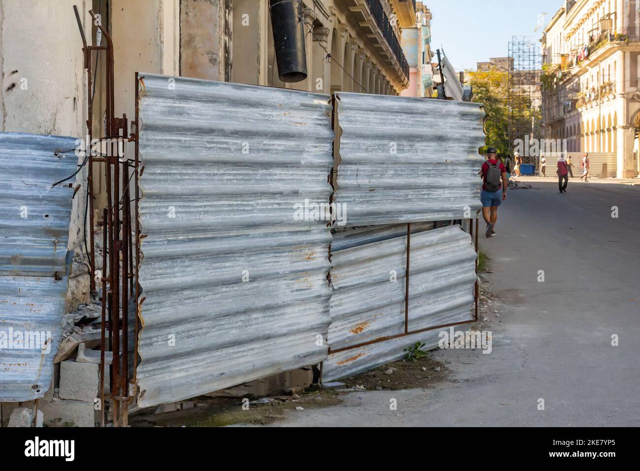 Una vieja valla metálica dilapidada protege un edificio en peligro de derrumbarse. Foto de stock