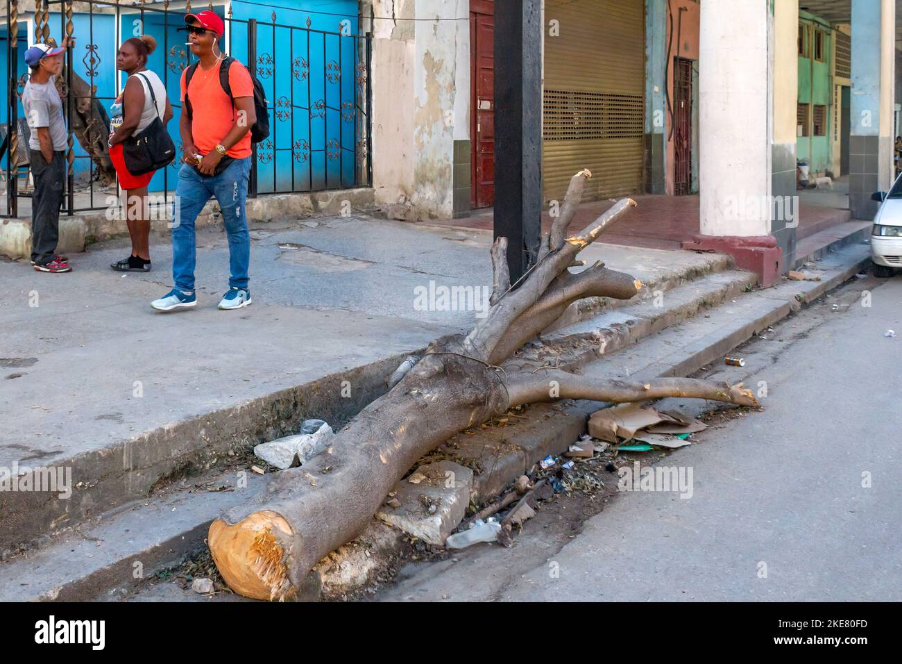 El pueblo cubano camina en una sucia acera donde un tronco de árbol todavía está colocado en la frontera de la calle Foto de stock