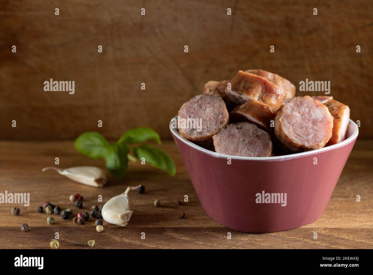 Rodajas de salchichas de cerdo ahumadas en cuenco con especias sobre fondo de madera Foto de stock