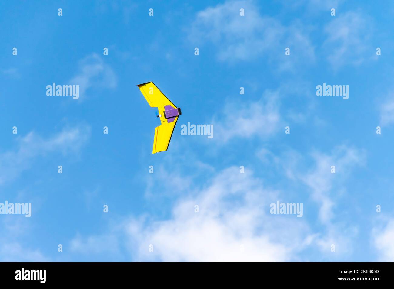 Aviones teledirigidos UAV volando con una hélice, de color amarillo y morado. Ángulo bajo con cielo azul nublado en el fondo Foto de stock