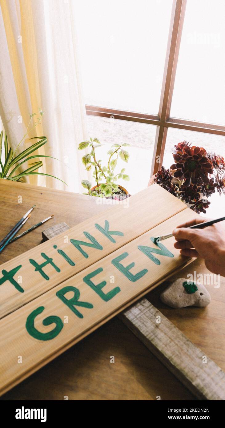 pintar y escribir con un pincel un signo de madera verde pensar para defender y apoyar el cuidado del planeta, el desarrollo sostenible y el medio ambiente Foto de stock