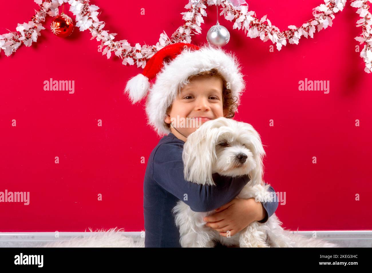 niño con sombrero de santa claus abrazando su perrito Foto de stock