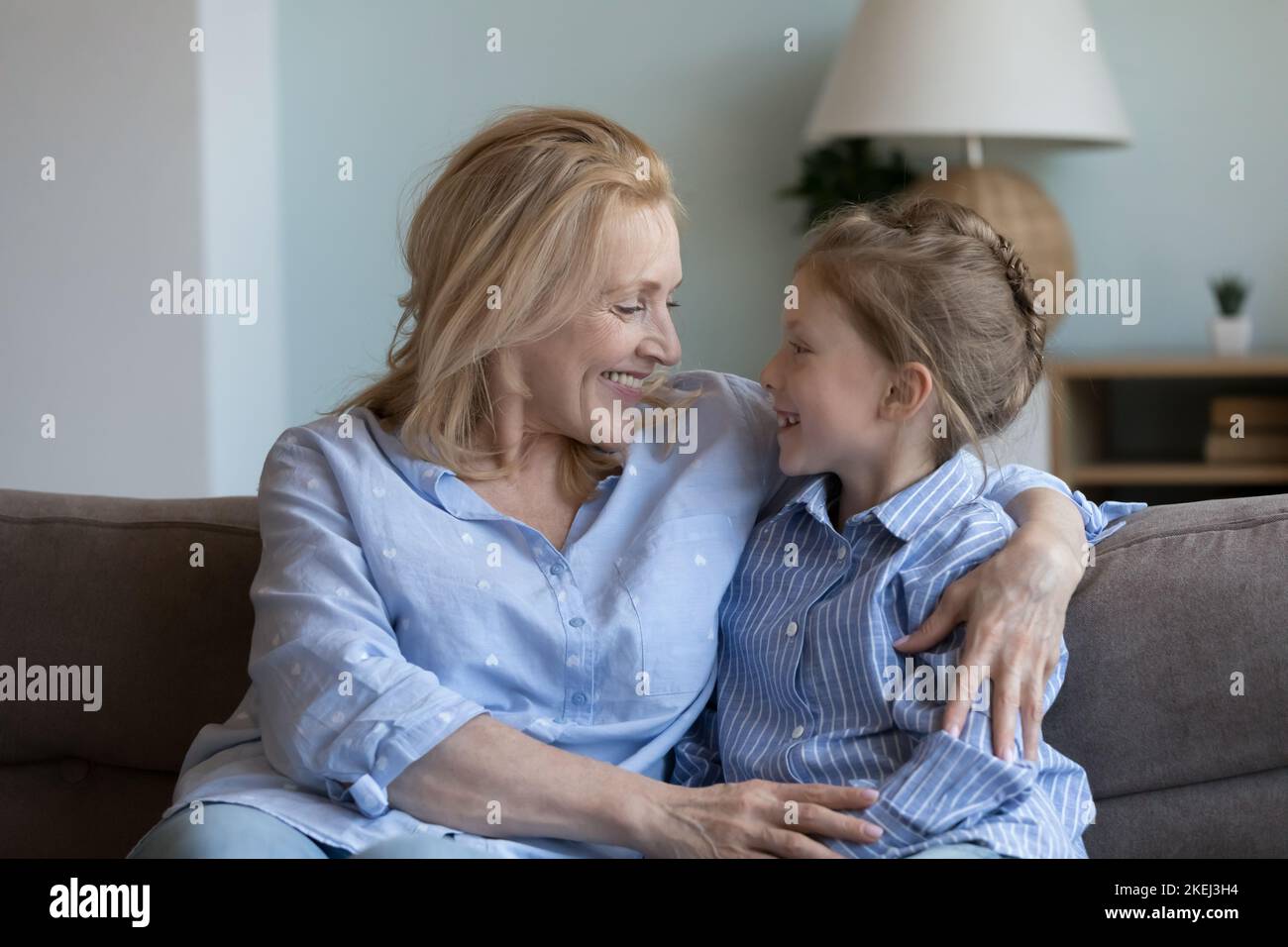 La abuela de mediana edad abraza a su nieta sentada en un sofá Foto de stock