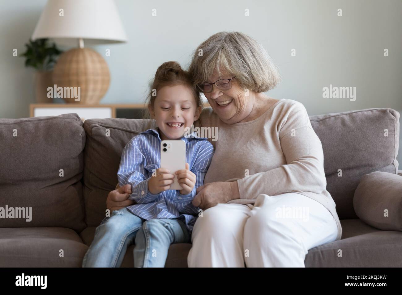 La chica pasa tiempo con la bisabuela en casa utilizando un smartphone moderno Foto de stock