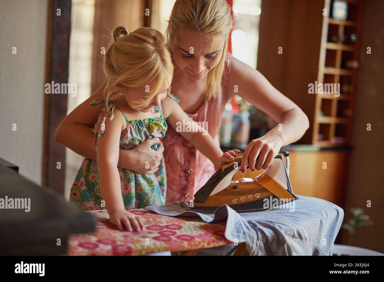 Ahora mira como los pliegues desaparecen como la magia. Una niña que ayuda a su madre a planchar algo de ropa. Foto de stock