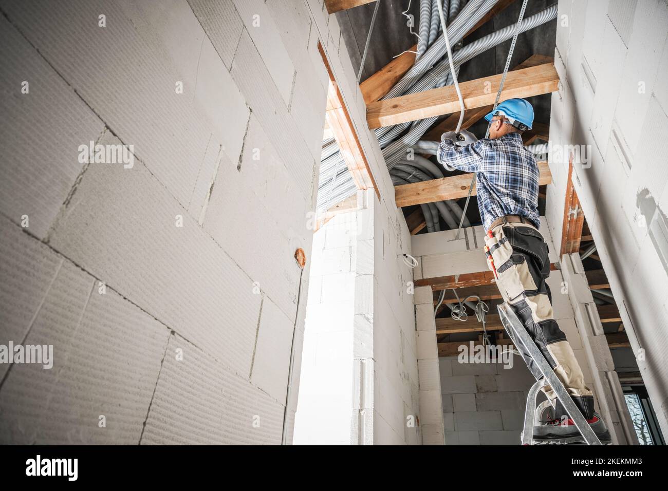 Electricista profesional Instalación de línea eléctrica a lo largo del techo en un edificio de hormigón de nueva construcción. Foto de stock