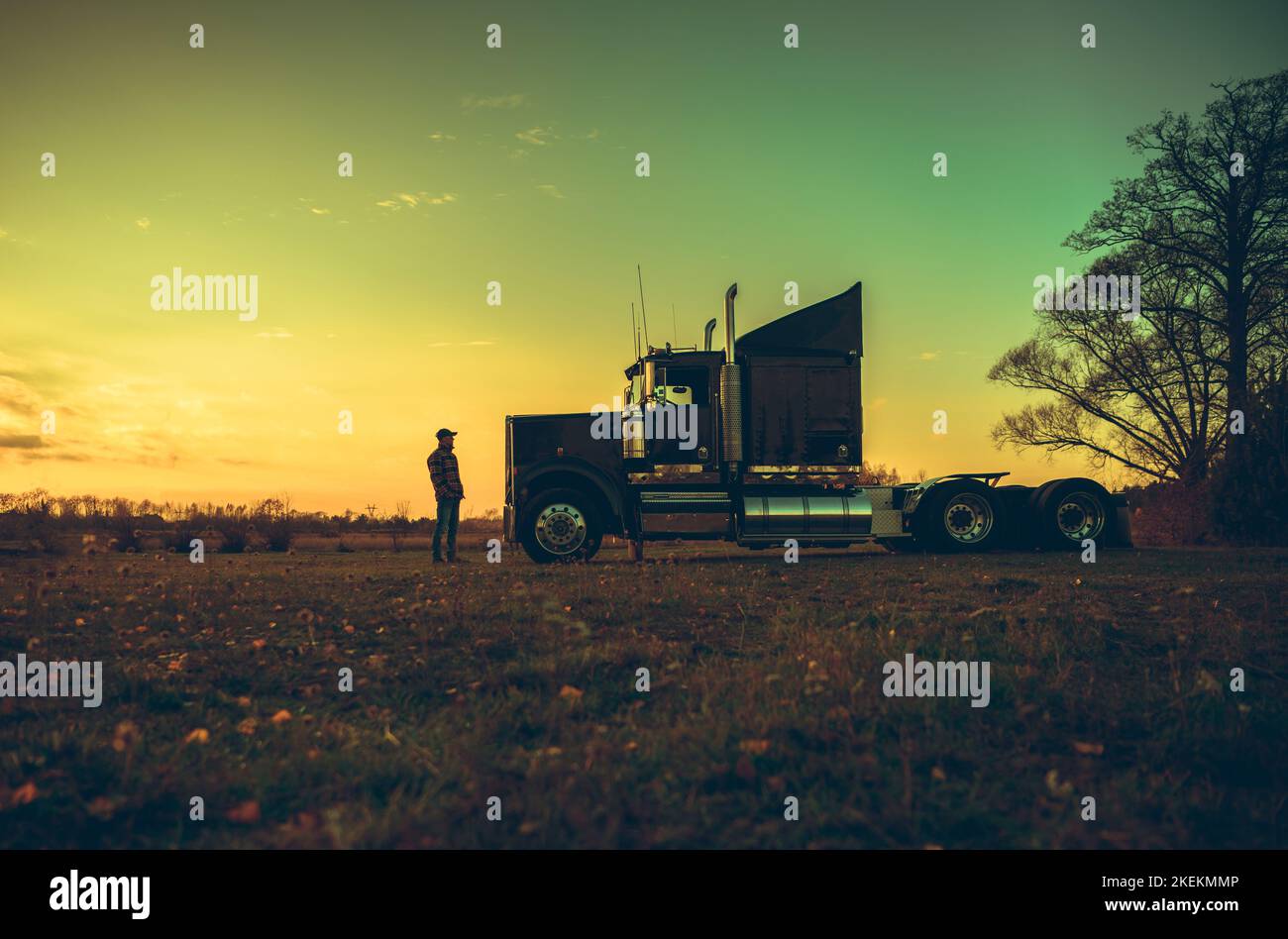 Conductor de semi camión delante de su vehículo durante la puesta de sol del campo escénico. Tema de la industria del transporte. Foto de stock