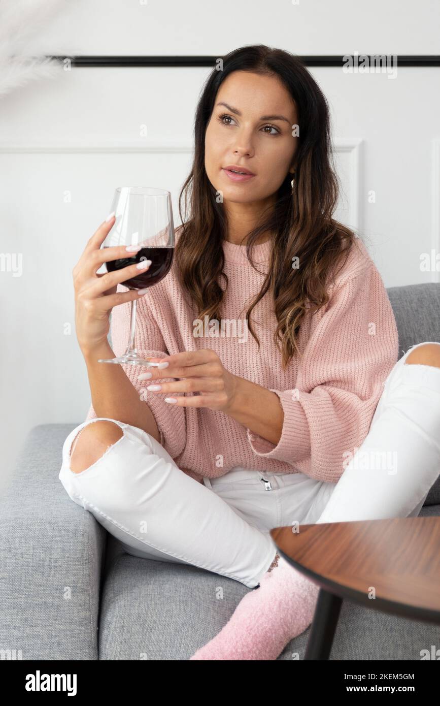 Mujer sentada en el sofá, descansando con una copa de vino tinto Foto de stock