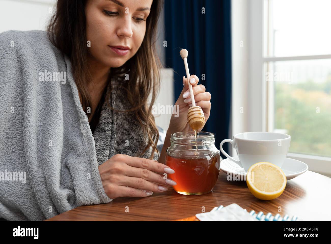 Mujer enferma poniendo miel en su té Foto de stock