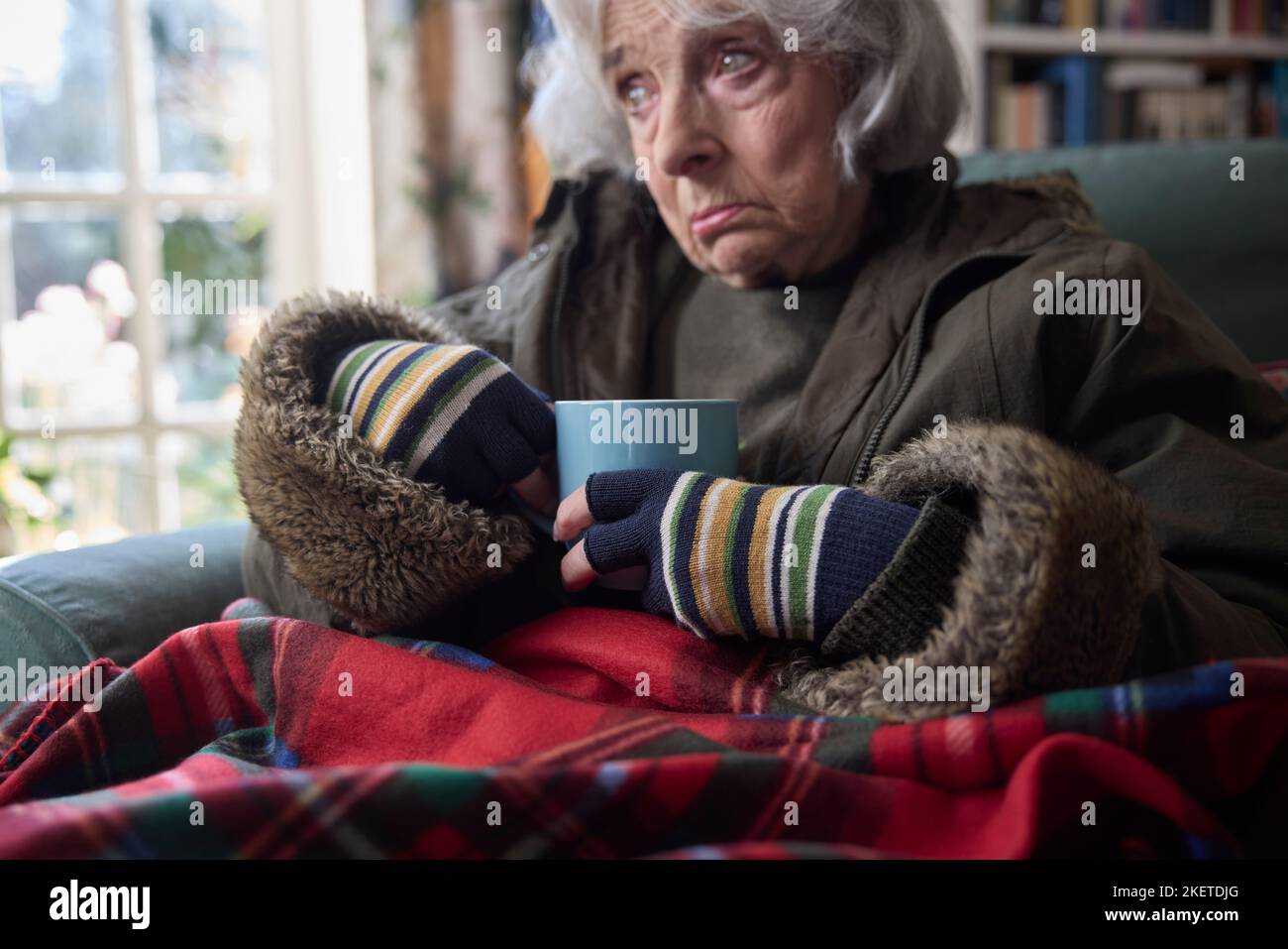 Primer plano de una mujer mayor que usa abrigo en interiores con bebida caliente Tratando de mantenerse caliente en casa en crisis de energía Foto de stock