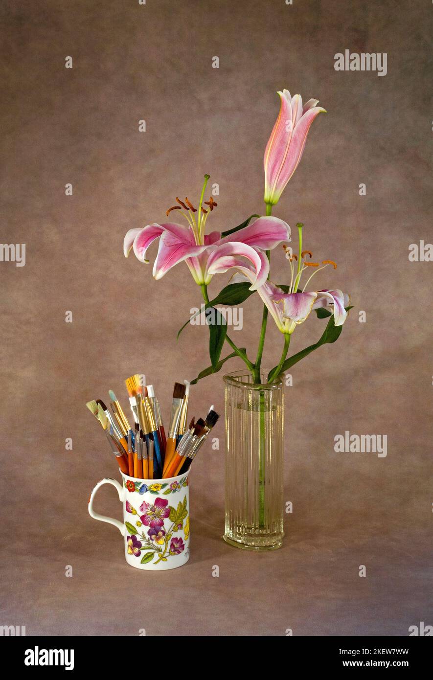 Una taza llena de pinceles de pintura de artista y un precioso ramo de lirios Stargazer en un jarrón. Foto de stock