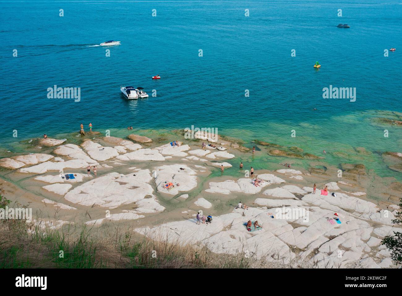 Sirmione playa, vista en verano de personas tomando el sol en Jamaica Beach en el borde norte de la península de Sirmione, Lago Garda, Lombardía, Italia Foto de stock