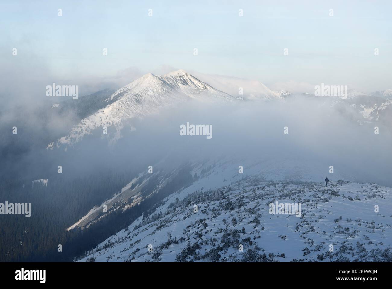 Paisaje de montaña de invierno con un pico nevado y un hombre en la cresta de la cresta en una caminata invernal extrema Foto de stock