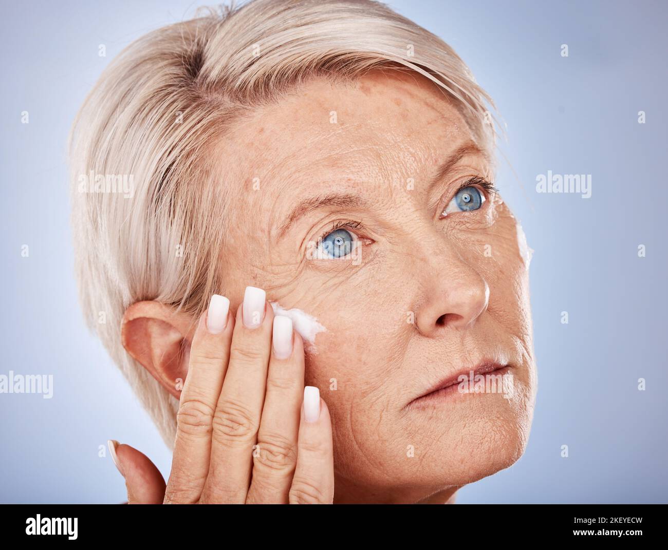 Mujer madura, crema y aplicar crema o loción para la cara de arrugas contra el envejecimiento sobre un fondo gris estudio. SPF, crema solar con una mujer mayor aplicar Foto de stock