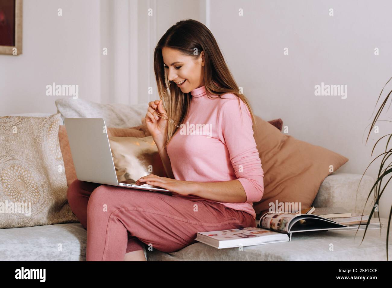 una niña por la mañana en pijama y gafas en casa trabaja en un portátil, una niña se autoaísla en casa y se apoya en el sofá y mira un portátil Foto de stock