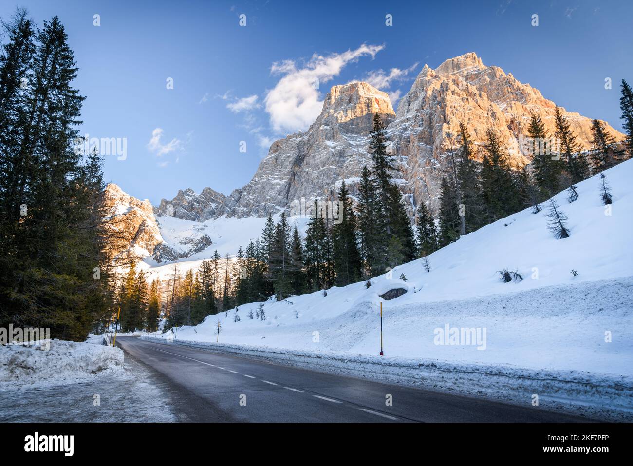 Tramo recto vacío de una carretera de montaña que corre al pie de un alto pico rocoso cubierto de nieve en un día claro de invierno Foto de stock