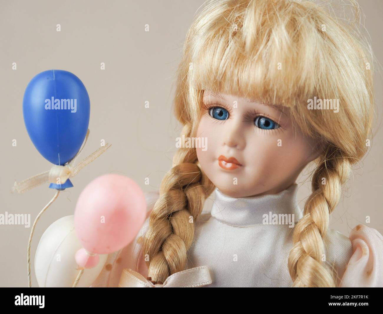 Muñeca de porcelana vintage rubia con trenzas con ojos azules en un vestido  ligero con globos blancos, rosados y azules Fotografía de stock - Alamy