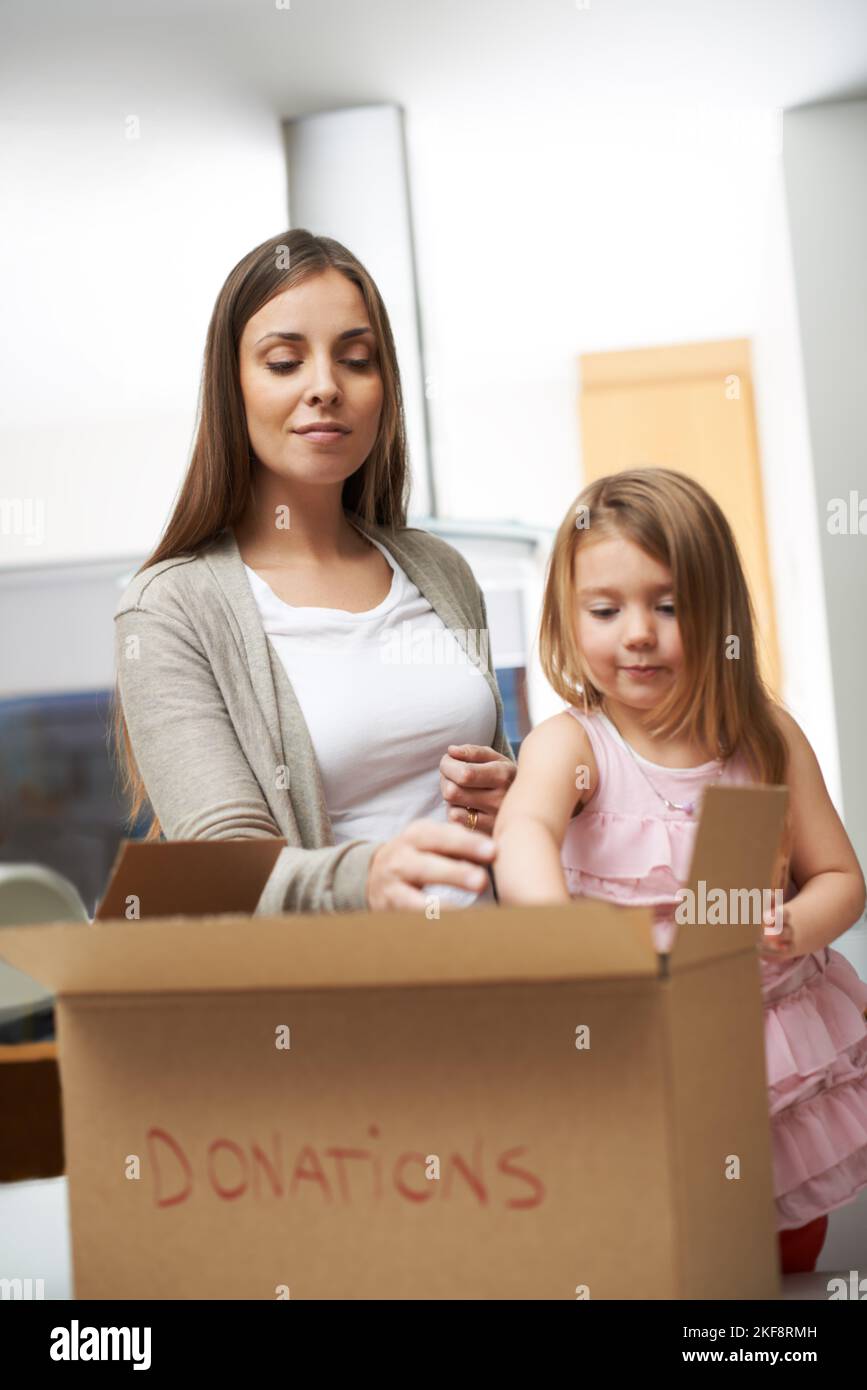 Estoy criando a una familia socialmente consciente. Una joven madre e hija embalando una caja de ropa para caridad. Foto de stock