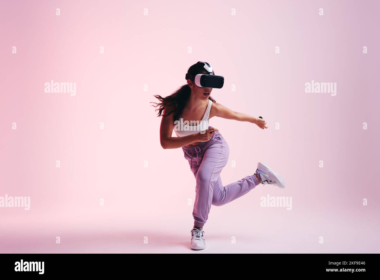 Mujer explorando el metaverso. Juego de mujer joven activa con gafas de realidad virtual y mandos. Mujer joven con energía teniendo una experiencia 3D en Foto de stock