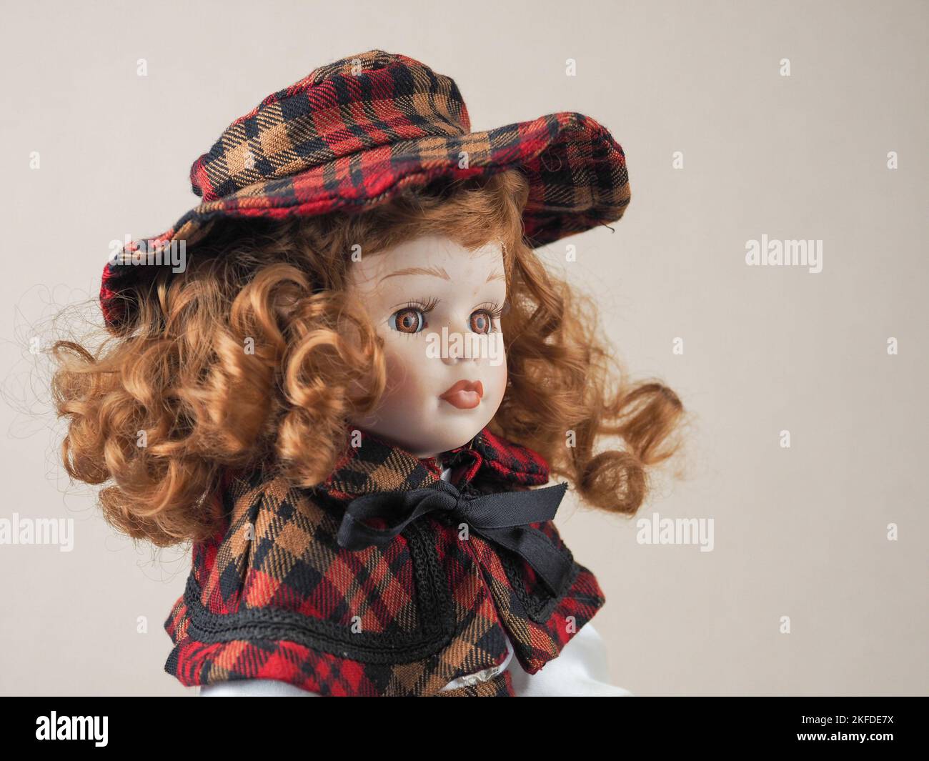 Chica muñeca de porcelana vintage con ojos marrones con pelo rizado rojo  que fluye en un vestido y un sombrero rojo y negro a cuadros. Muñecas de  porcelana aparecieron en el siglo