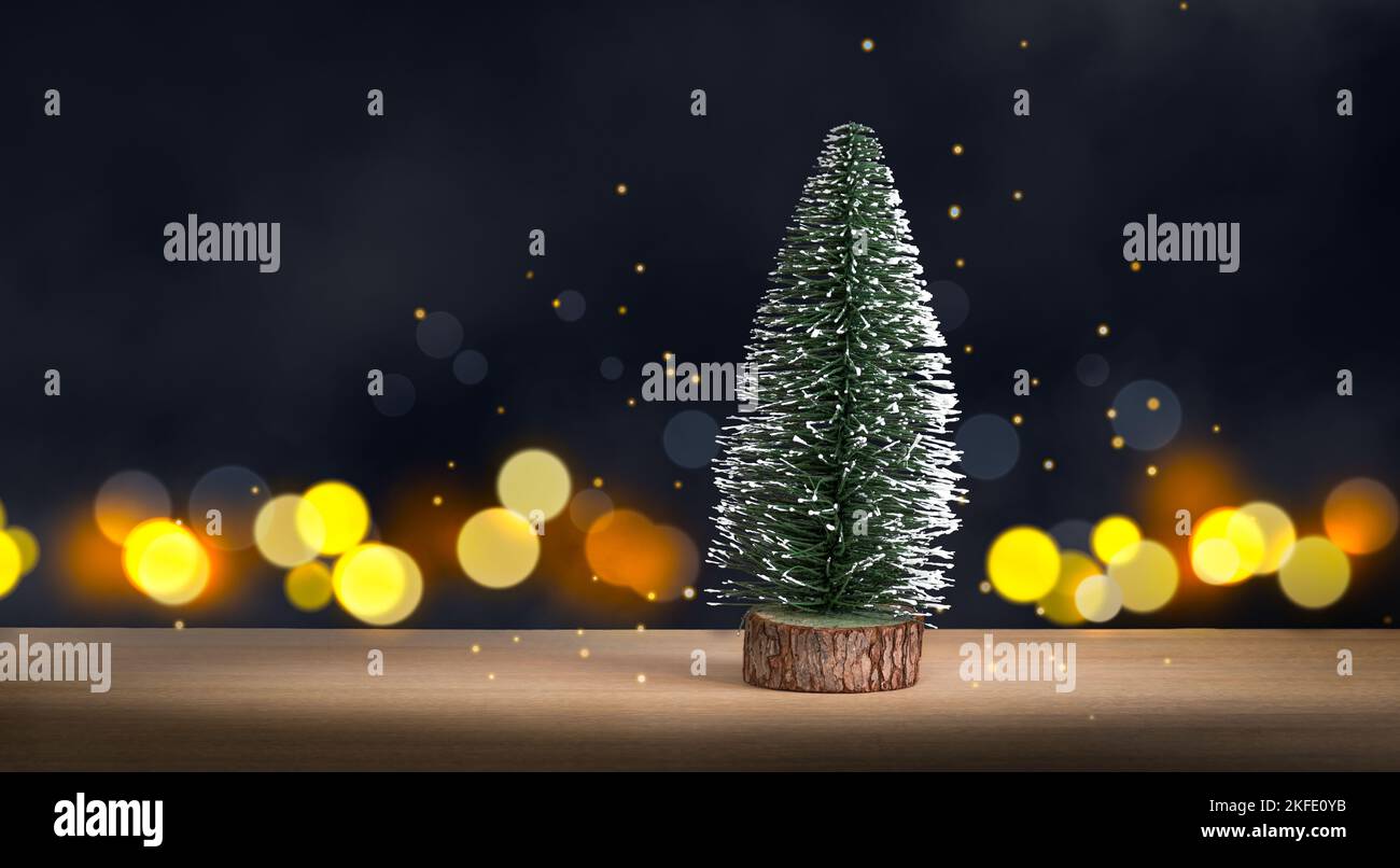 Pequeño árbol de Navidad sobre madera, sobre fondo oscuro de luces desenfocadas. Foto de stock