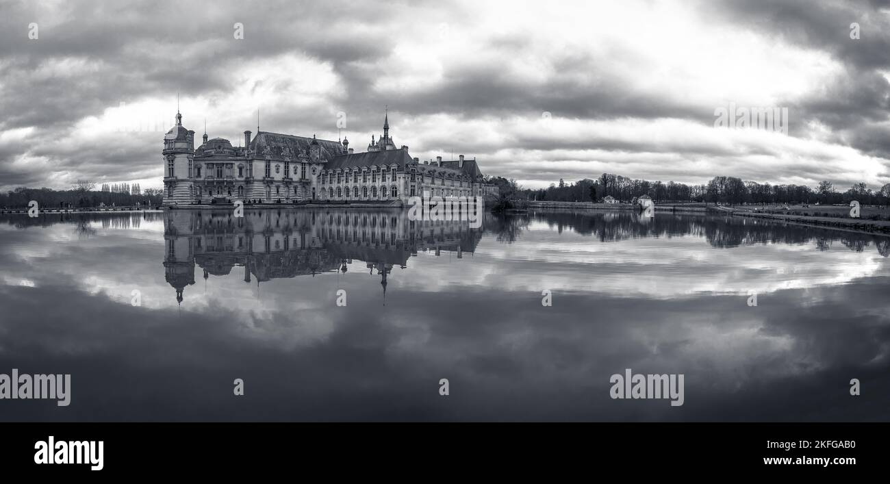 Domaine de Chantilly, Castillo de Chantilly al atardecer, reflexión del cielo nublado en el estanque. Famoso destino turístico cerca de París. Foto de stock