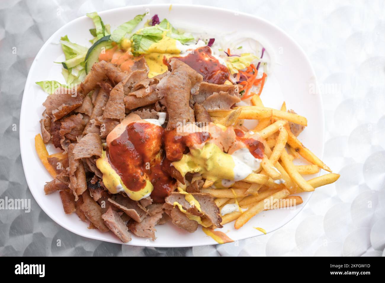 Doner kebab en un plato con patatas fritas, ensalada y varias salsas