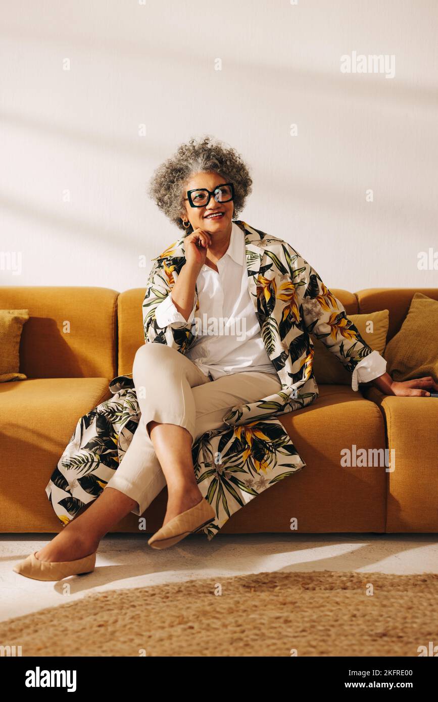 Mujer de negocios pensativa mirando con una sonrisa mientras se sienta en un sofá en el vestíbulo de una oficina. Pensativa empresaria trabajando en un coworking creativo Foto de stock