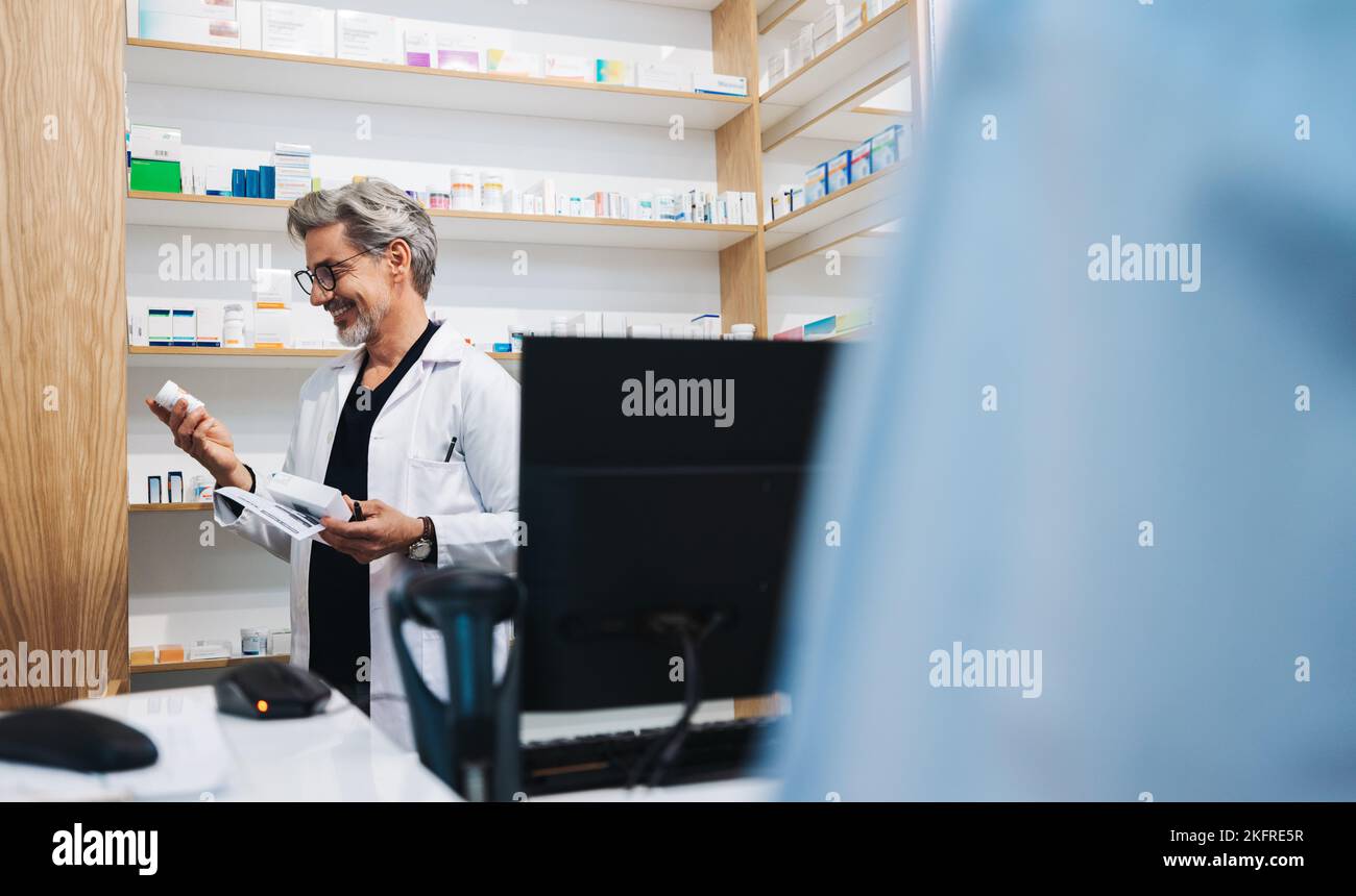 Farmacéutico maduro que lee la etiqueta de la medicación mientras que asiste a un paciente en una tienda de la droga. Profesional de la salud que dispensa una receta médica en un Foto de stock