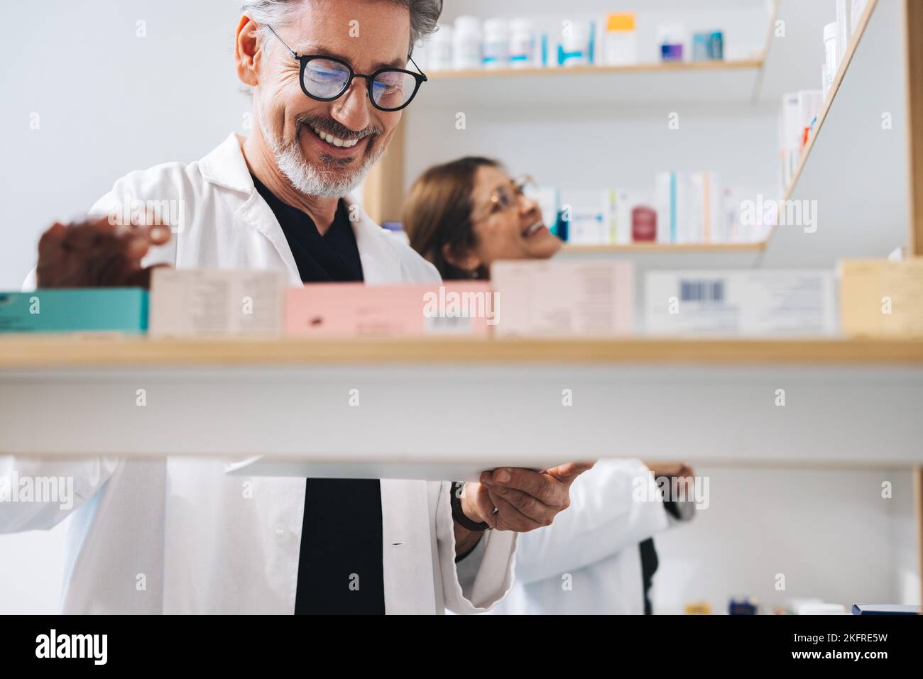 Farmacéutico masculino que recoge los medicamentos recetados en una farmacia. Hombre senior feliz trabajando en una farmacia con su colega. Foto de stock