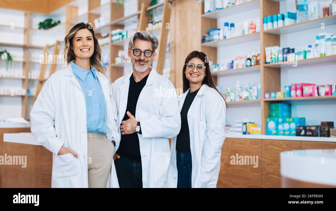 Tres farmacéuticos juntos y mirando la cámara en una farmacia. Grupo de profesionales de la salud que trabajan en una farmacia. Foto de stock