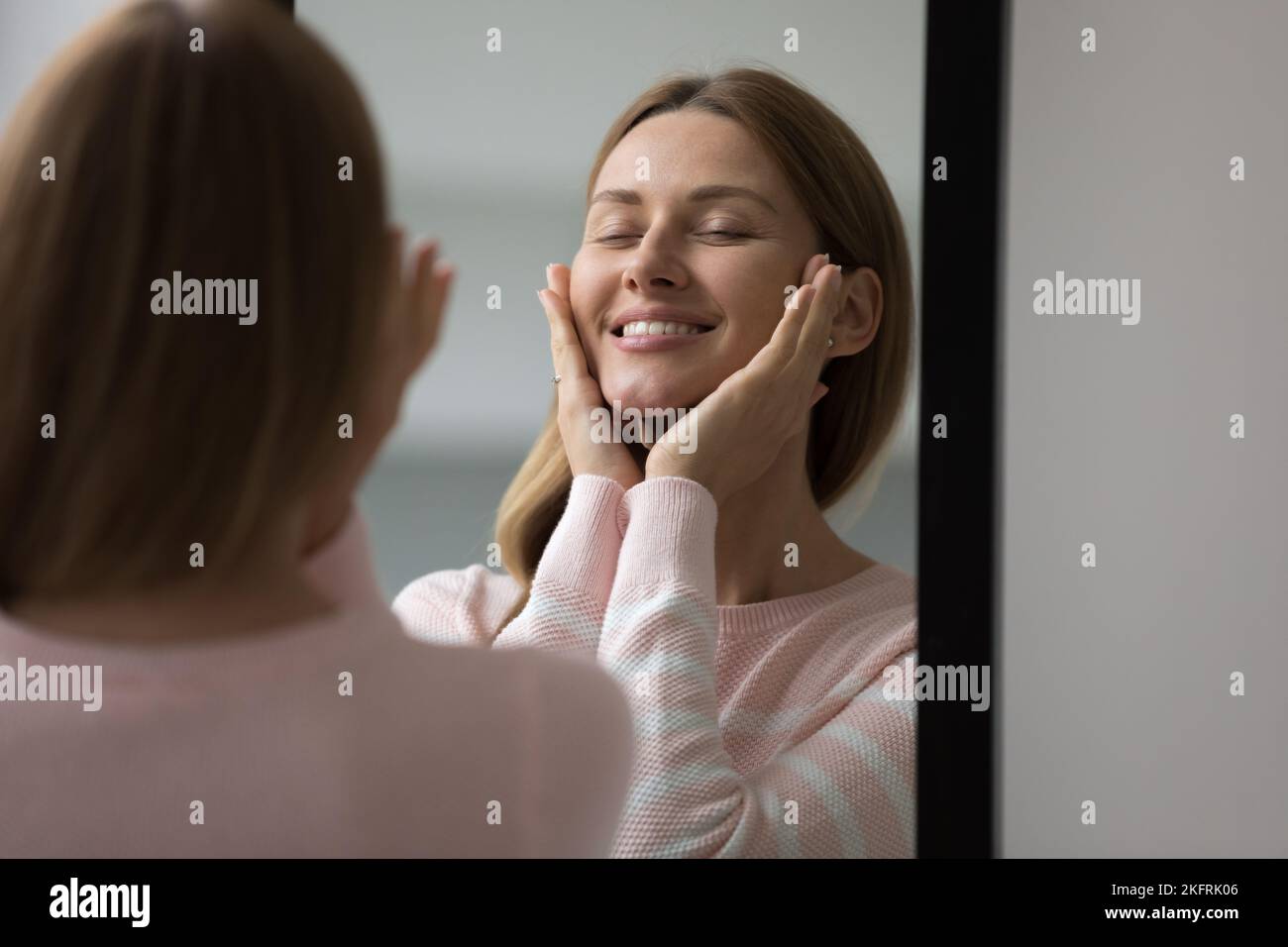 Una joven atractiva mira el espejo, toca su rostro perfecto Foto de stock