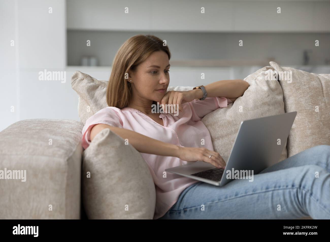 Mujer hacer compras electrónicas sentado en un sofá con ordenador portátil Foto de stock