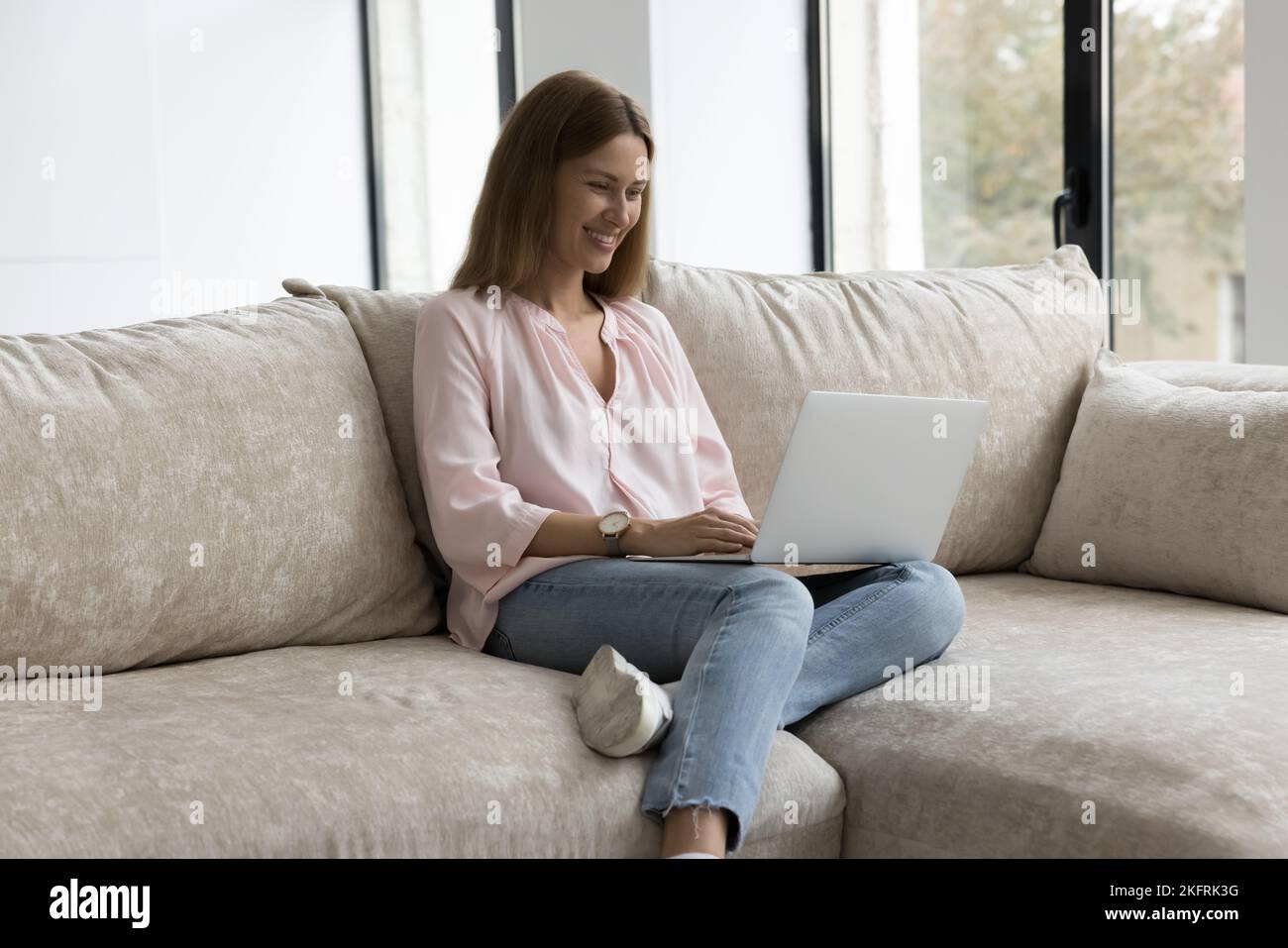 Sonriente mujer milenaria Relájese en el sofá con un moderno ordenador portátil Foto de stock