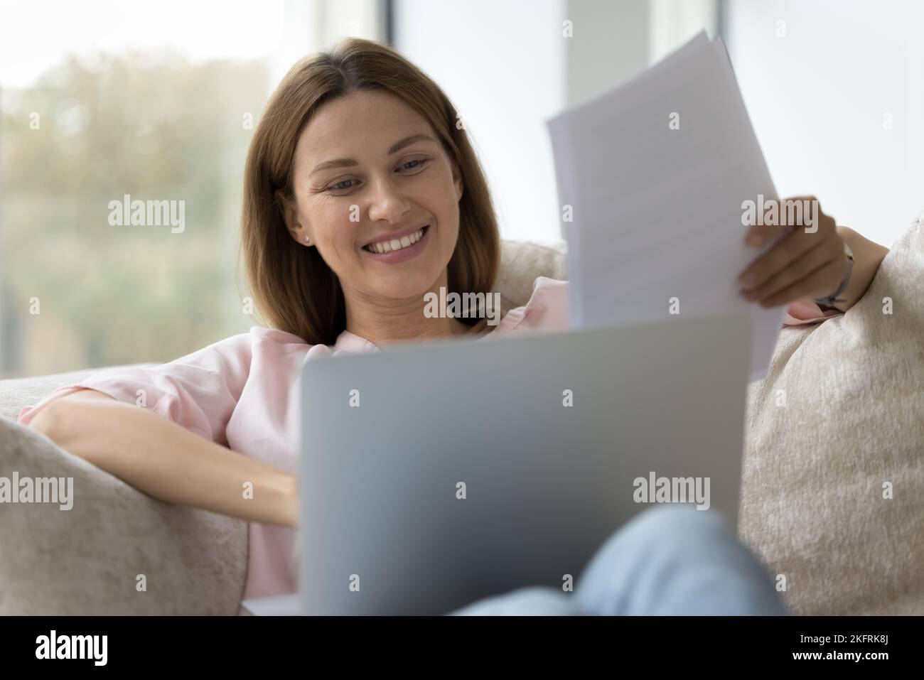 Una mujer sonriente sostiene los papeles sentados con el ordenador en las vueltas Foto de stock