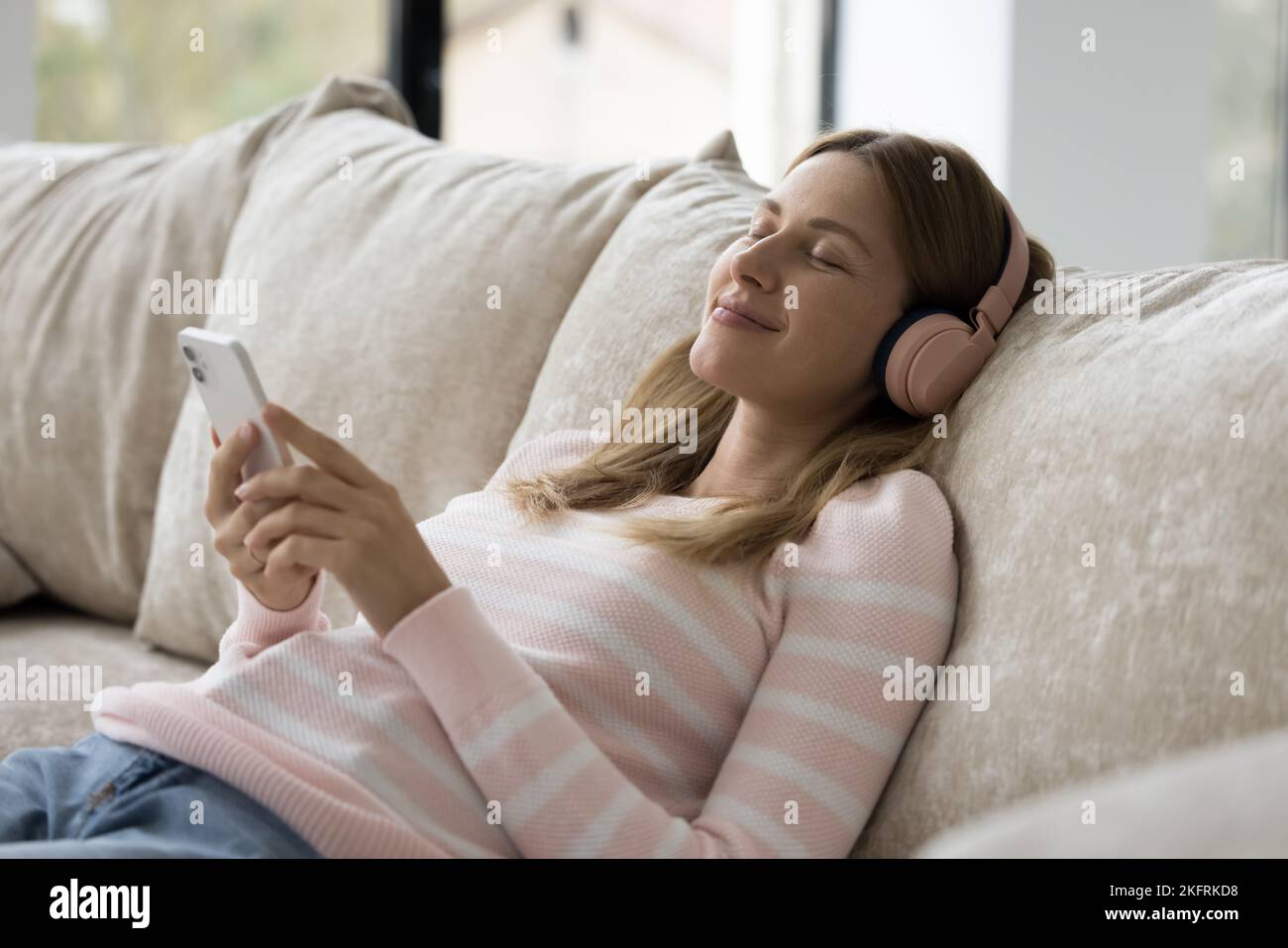 Mujer serena sujeta smartphone Disfruta de la música a través de los auriculares inalámbricos Foto de stock