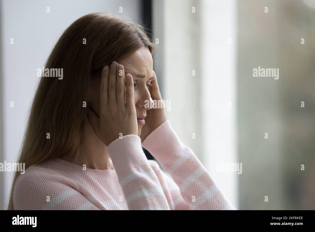 De cerca: Una mujer joven de pie en interiores sufre un fuerte dolor de cabeza Foto de stock