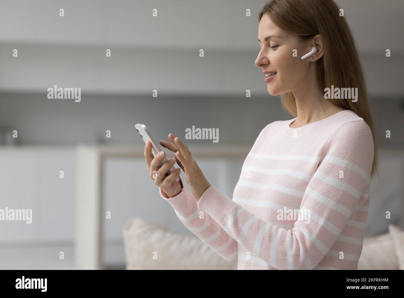 Mujer en auriculares inalámbricos sostiene smartphone elegir música Foto de stock