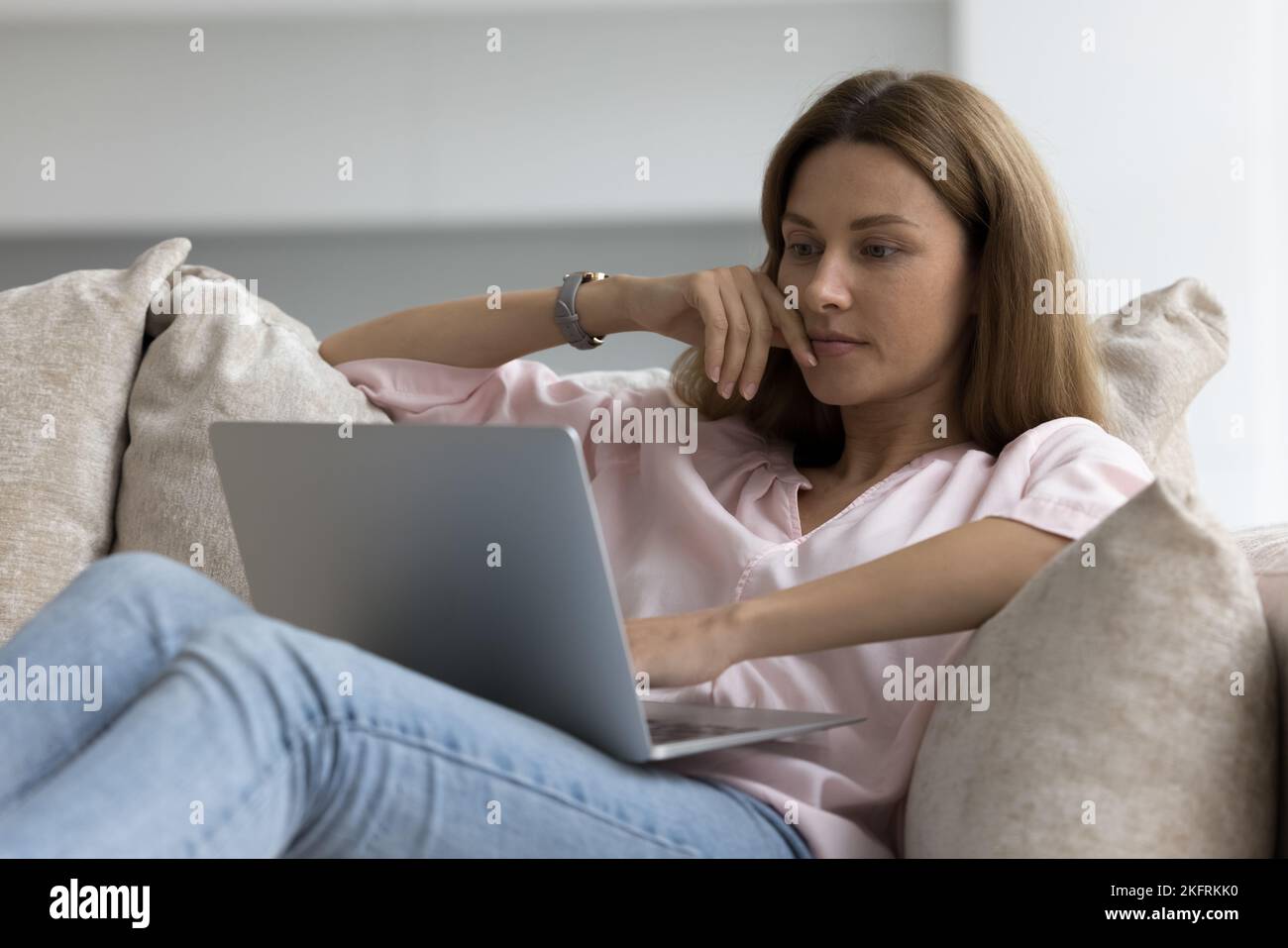 Mujer joven seria y pensiva sentada en el sofá con el ordenador portátil Foto de stock